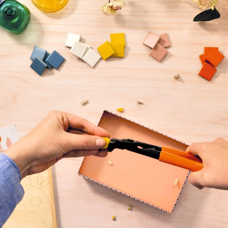 Person using a tool to cut a piece of leather on a wooden surface with colorful blocks around.