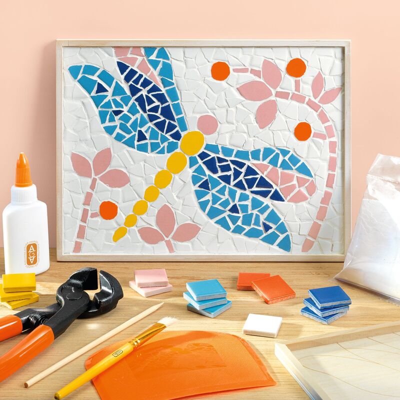 Mosaic dragonfly art project with tools and materials on a wooden surface