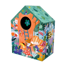 A whimsical house-shaped wooden birdhouse or decorative box with a colorful illustrated forest scene, including a cat in a window, a ladder, flowers, mushrooms, and a gold-tone lock on the front.