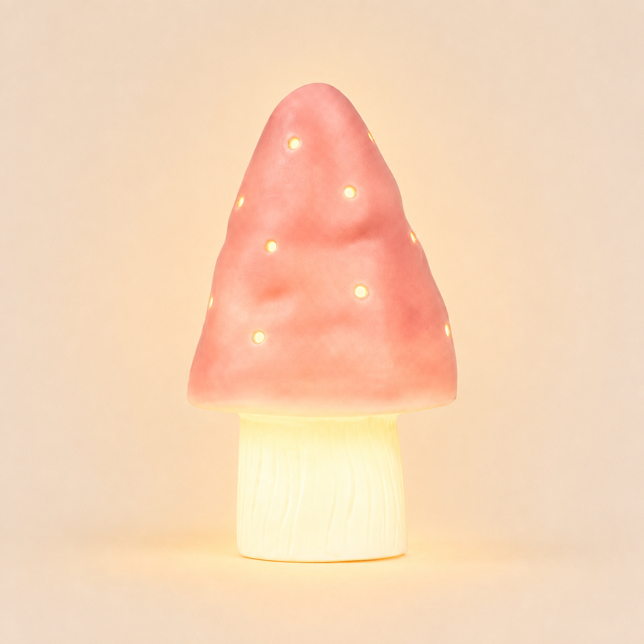 A mushroom-shaped night light with a pink textured cap featuring small cutout dots that glow warm yellow, mounted on a cream-colored wood-textured base, set against a solid beige background.