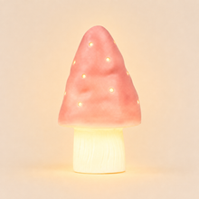 A mushroom-shaped night light with a pink textured cap featuring small cutout dots that glow warm yellow, mounted on a cream-colored wood-textured base, set against a solid beige background.