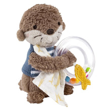 A plush toy otter holding a colorful rattle ring with beads in its handle, designed for babies and toddlers.