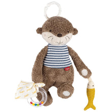 A plush toy representing an otter with a striped blue and white shirt, holding a yellow fish, and attached to a white C-ring for hanging.