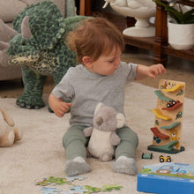 A child sitting on the floor playing with a wooden racing slide toy, surrounded by soft toys and a puzzle.