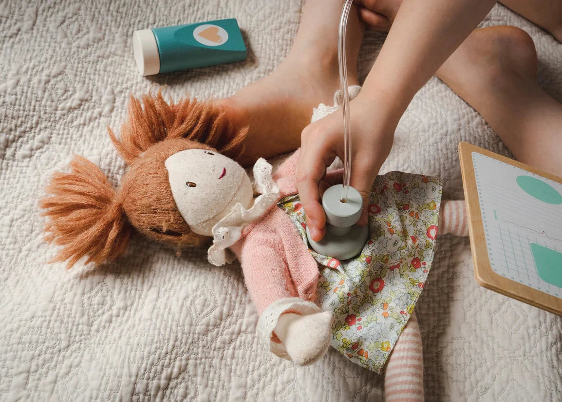 Child playing with a doll and toy stethoscope on a bed