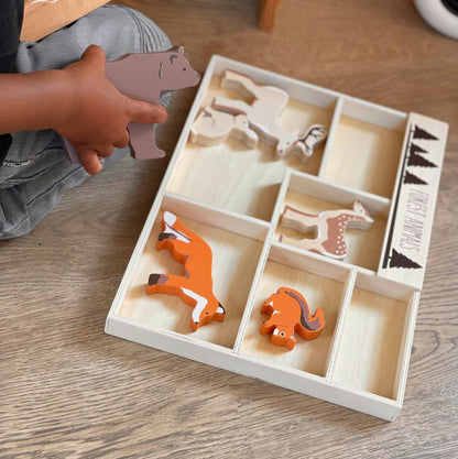 Child playing with wooden animal toys in a box on a wooden floor.