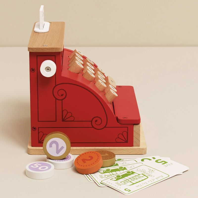 Wooden toy cash register with coins and cards on a beige background