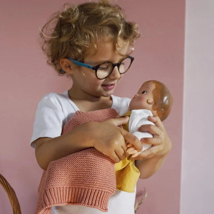 Child holding a baby doll against a pink background