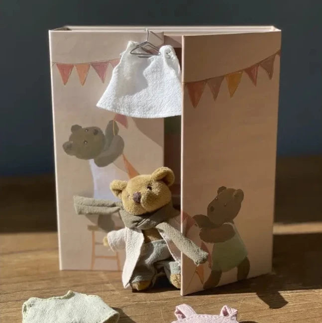 Small teddy bear with clothes in front of a cardboard box with teddy bear illustrations.