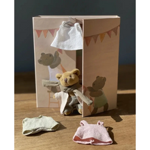 Small teddy bear with clothes in front of a cardboard box with teddy bear illustrations.