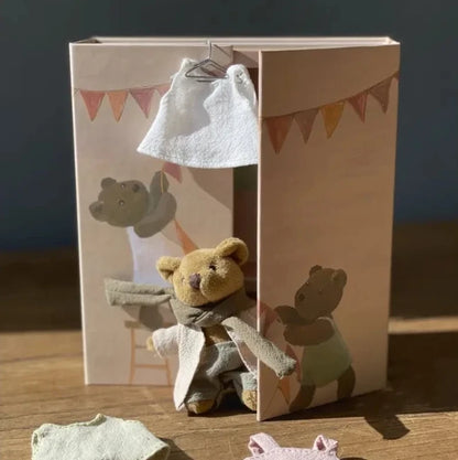 Small teddy bear with clothes in front of a cardboard box with teddy bear illustrations.