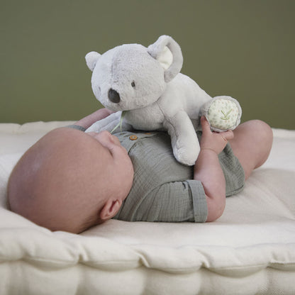 Baby lying on a white mattress cuddling a grey koala soft toy
