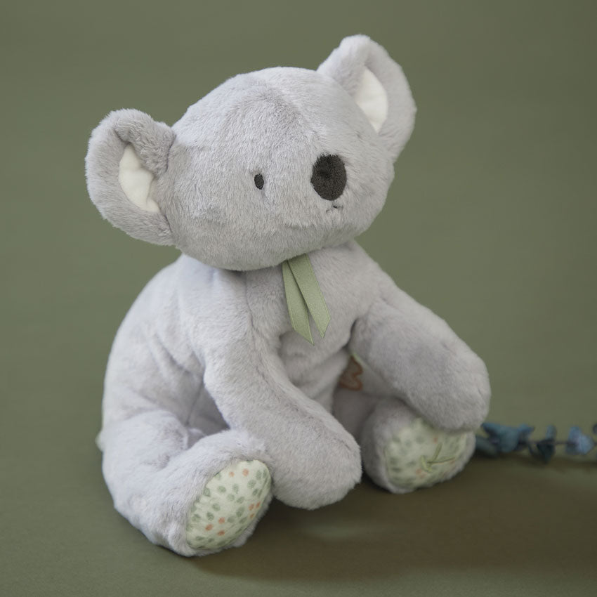 Grey koala soft toy with green neck bow sitting on a sage green bakground