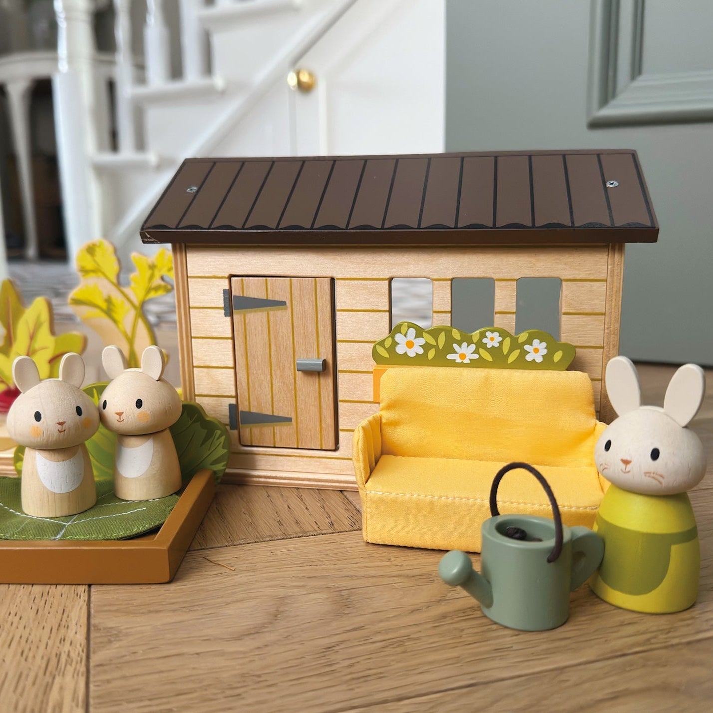Wooden toy set with a house, furniture, and animals on a wooden floor.