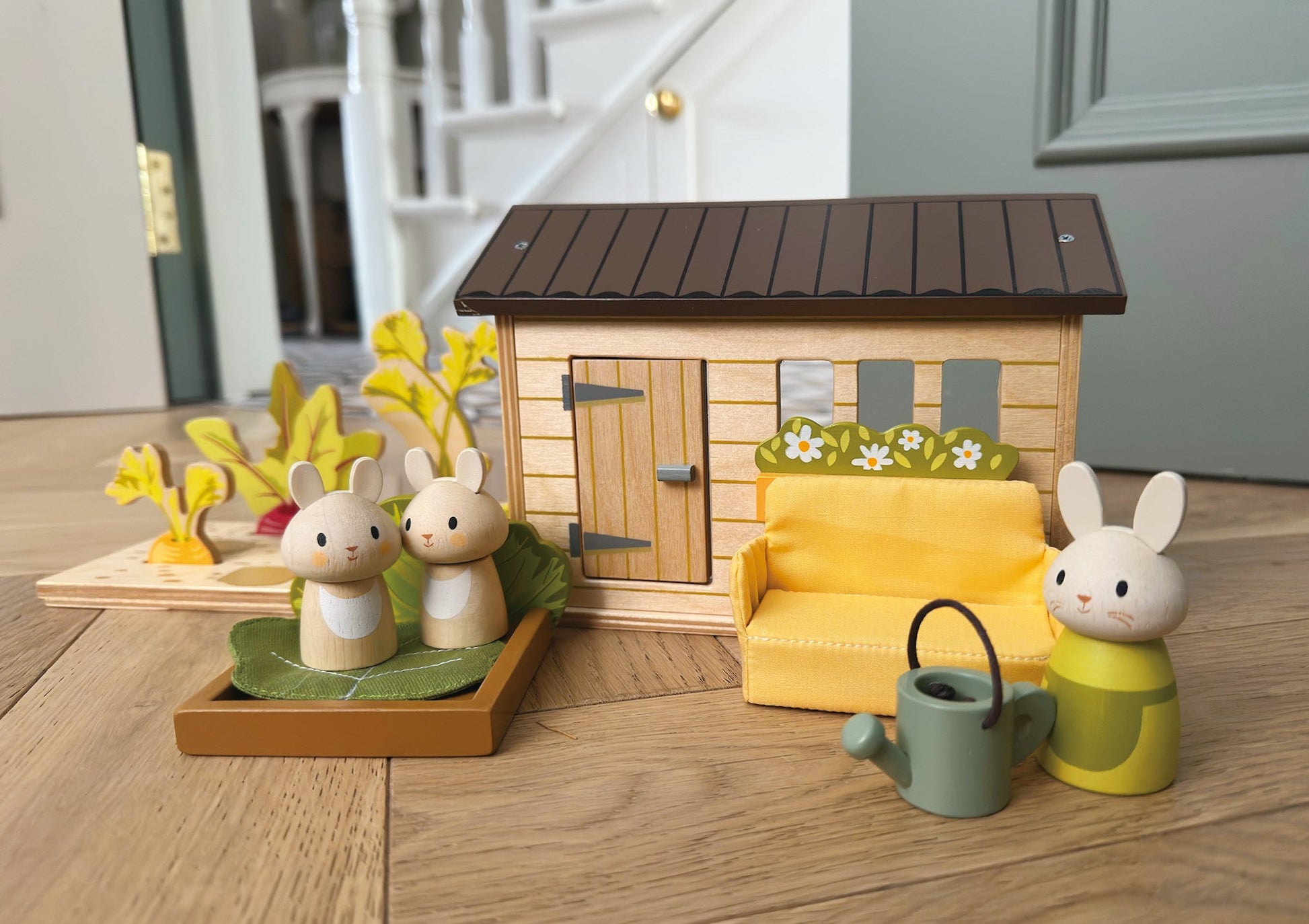 Wooden toy set with a house, furniture, and animals on a wooden floor.