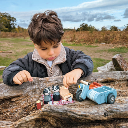 Child playing with toy cars and badger figures on a log outdoors