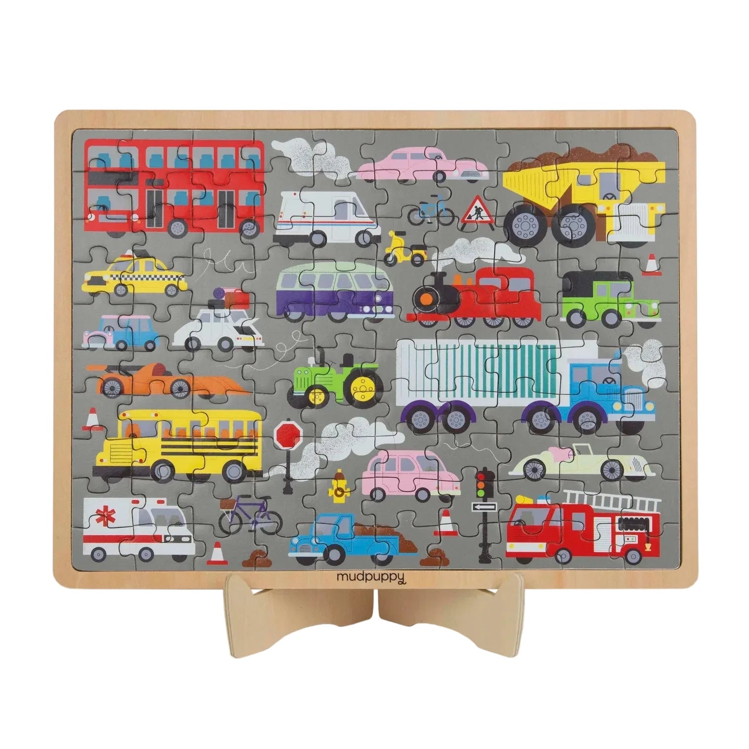 A children's wooden traffic-themed jigsaw puzzle displayed on a small wooden stand. The puzzle features a gray background with various colorful vehicles including a red double-decker bus, yellow dump truck, school bus, ambulance, fire truck, train, and cars, with the brand name 'mudpaisley' printed at the bottom.