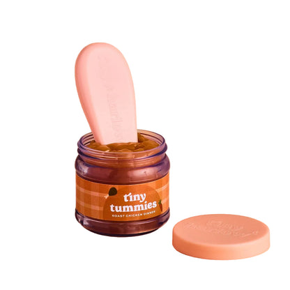 Jar of 'tiny tummies' baby doll pretend play food with a pink spoon on a beige background