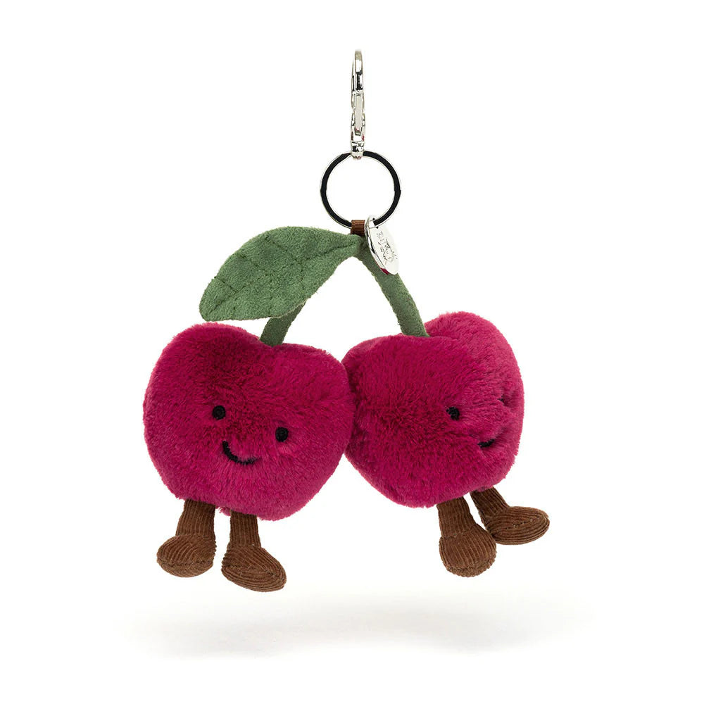 A plush toy resembling two cherries with faces, legs, and a green leaf on a silver clasp.