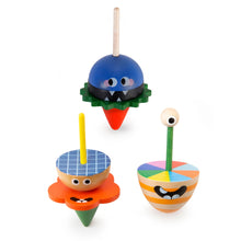 A collection of four wooden spinning tops with different monster designs and colors. Each top has a wooden stick handle and a colorful spinning top part.