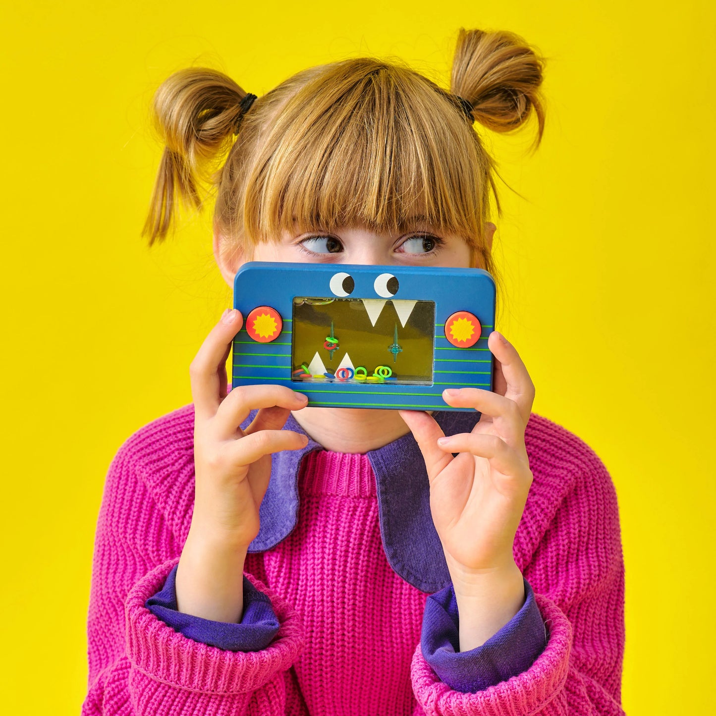 Young girl wearing bright pink jumper, holding blue  Kidoki wooden water game
