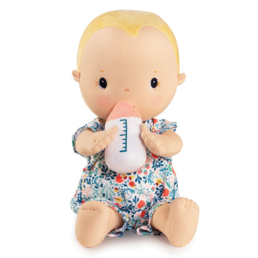 A soft body doll resembling a baby with a feeding bottle and a floral romper.