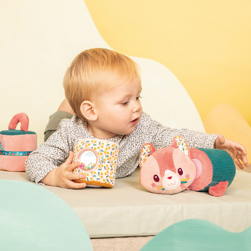 Child playing with a plush toy and a container on a light-colored surface with a yellow background