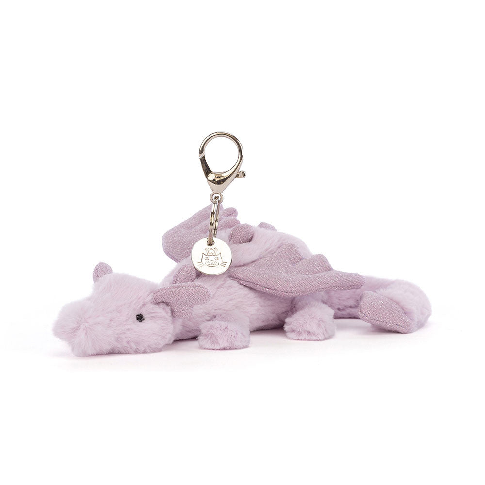 A soft purple dragon bag charm with a silver claw clip and a Jellycat tag, featuring tiny wings, a curved tail, and sparkling accents on the face and body.