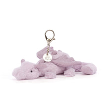 A soft purple dragon bag charm with a silver claw clip and a Jellycat tag, featuring tiny wings, a curved tail, and sparkling accents on the face and body.
