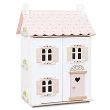 A white doll house with pink accents and a scalloped roof, featuring gold heart motifs and a pink door with a heart shape on it.