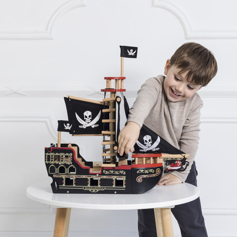 Child playing with a wooden pirate ship toy on a white surface.