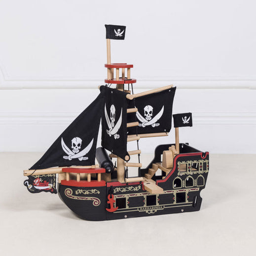Wooden pirate ship model with flags on a white surface and light gray background