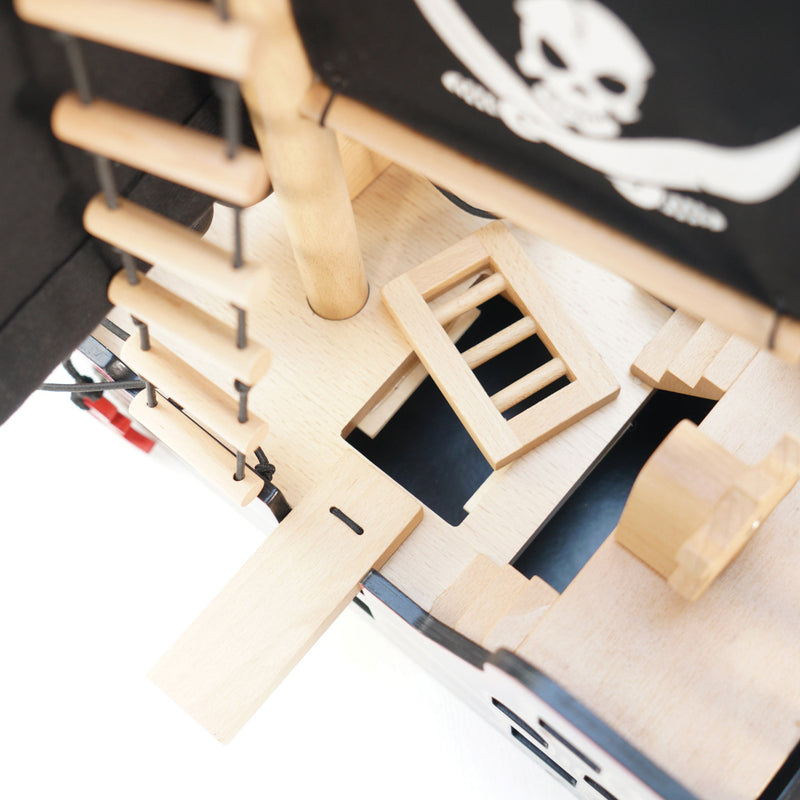 Close-up of a wooden model ship with a pirate flag in the background