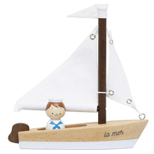A wooden sailing boat toy with a small figurine of a sailor, primarily beige and white with walnut-stained parts.