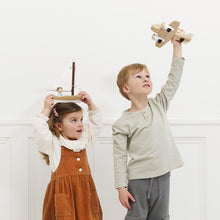 Two children playing with wooden toys against a white wall.