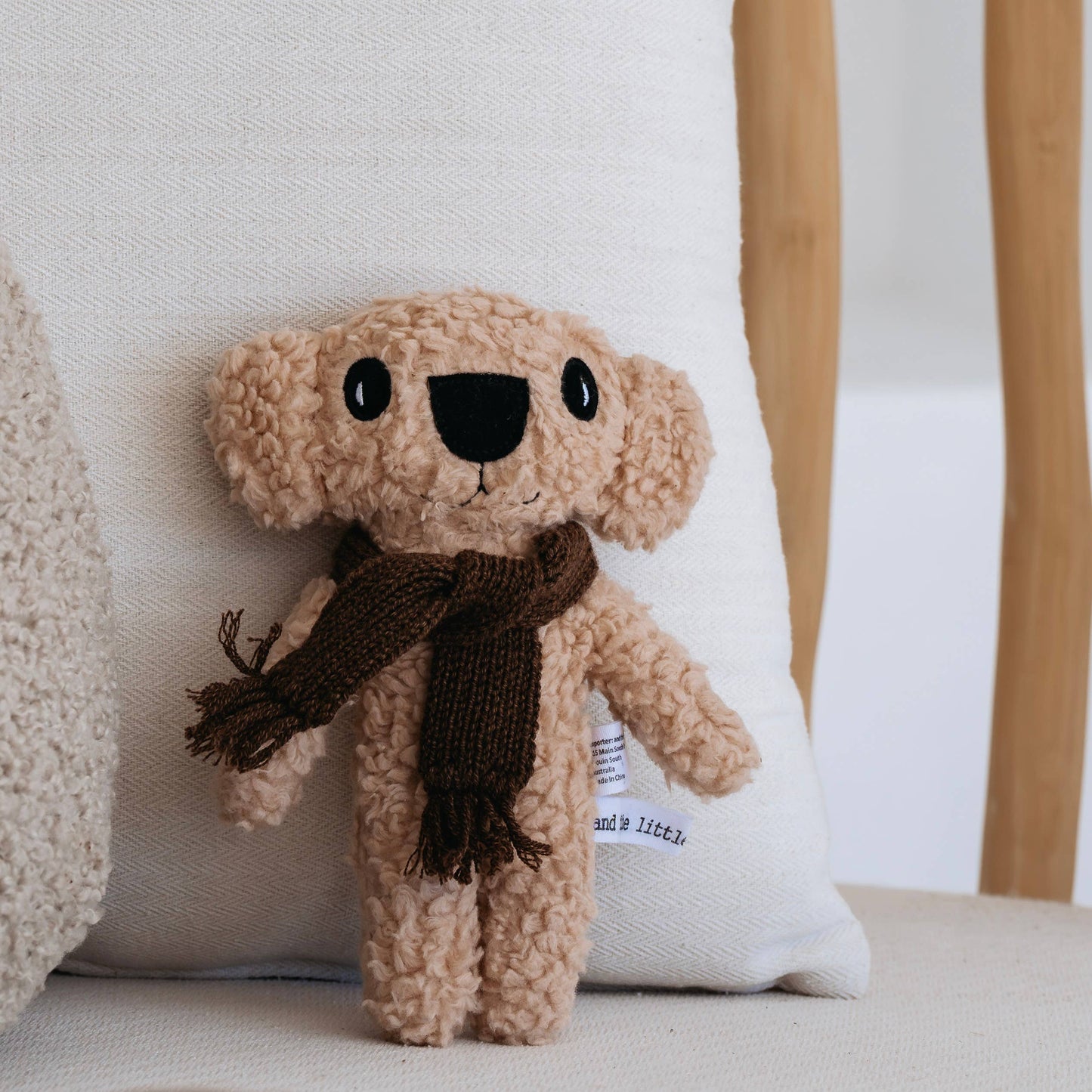 Knitted koala teddy bear with a brown scarf on a white cushion
