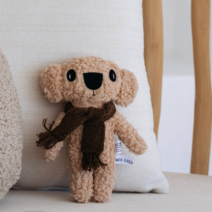 Knitted koala teddy bear with a brown scarf on a white cushion