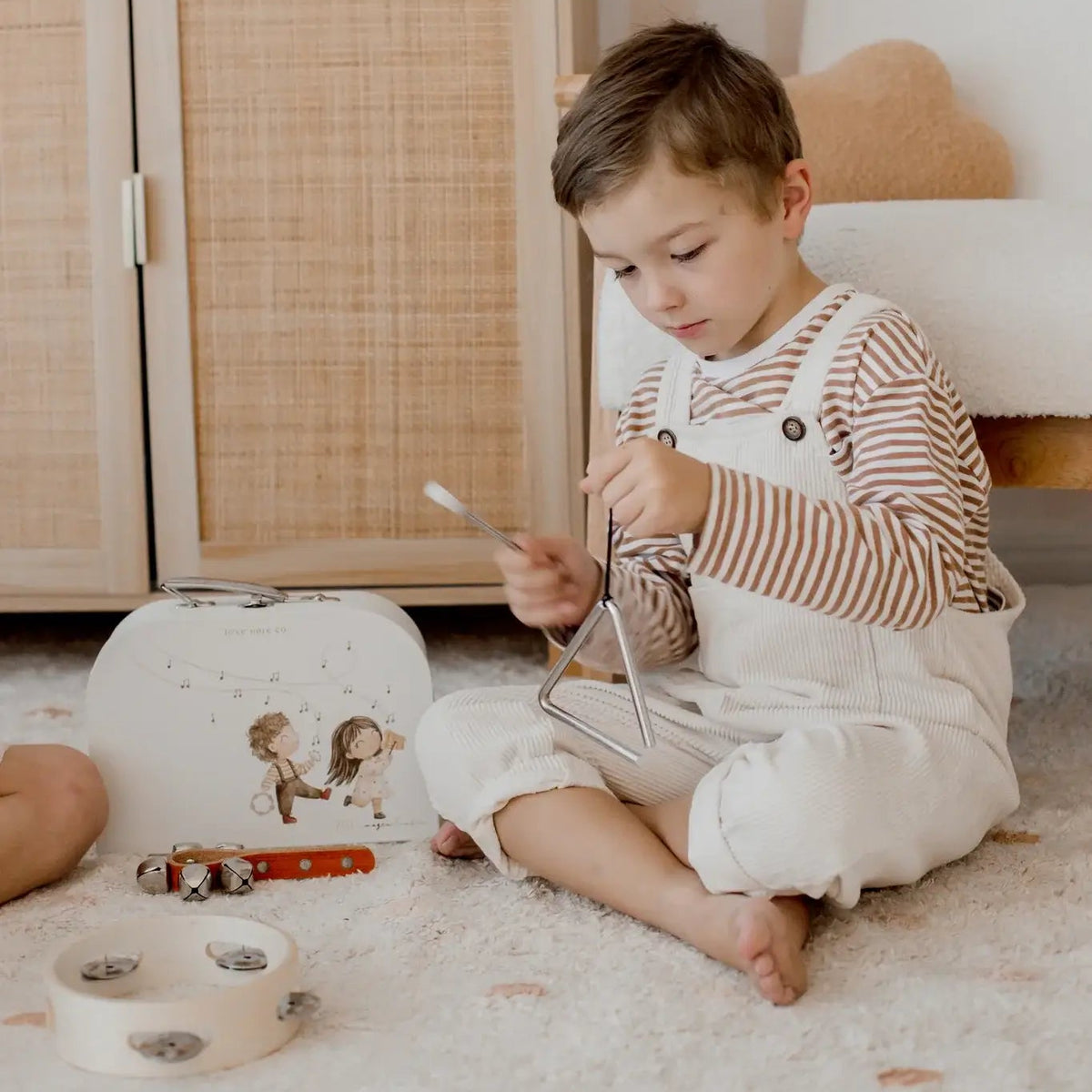 Toddler playing the triangle from the Love Note Co Little Sounds Music Set in a nursery.