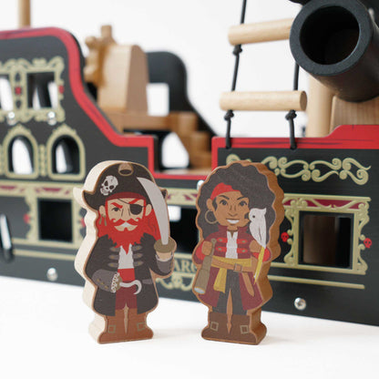 Two wooden pirate figures in front of a toy pirate ship.