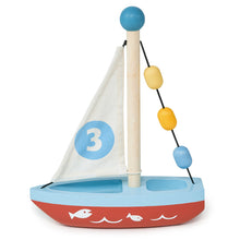 A wooden toy boat with a blue deck, red lower part, and a white sail with the number 3 printed on it. The boat has a mast with colorful beads and decorative elements.