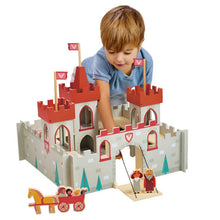 A child playing with a wooden toy castle set with figures including soldiers, a king, and a queen.