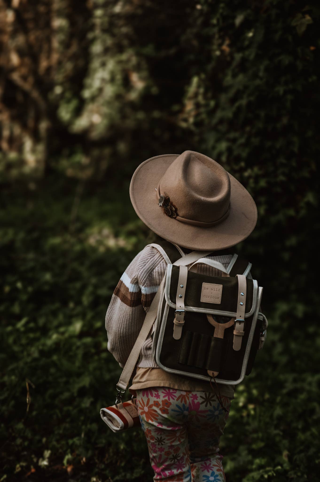 Child wearing a hat and backpack in a forest setting