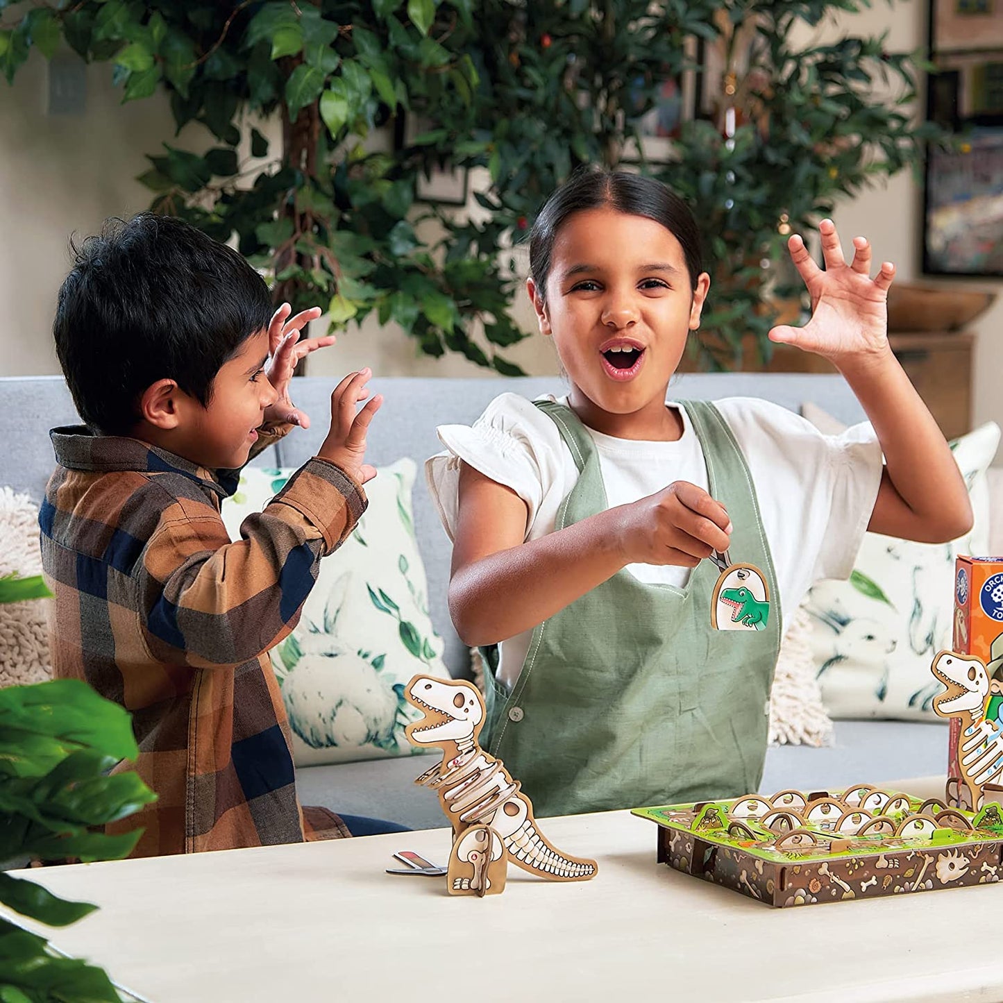 Two children playing with dinosaur toys on a table, surrounded by plants.