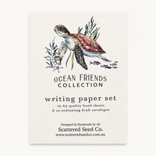A vertical paper card or packaging insert for a writing paper set, featuring an illustrated sea turtle with seaweed and small fish above the text 'OCEAN FRIENDS COLLECTION' and 'writing paper set.' The card is photographed against a plain light background.