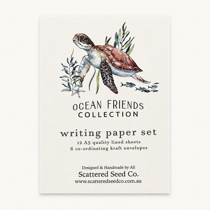 A vertical paper card or packaging insert for a writing paper set, featuring an illustrated sea turtle with seaweed and small fish above the text 'OCEAN FRIENDS COLLECTION' and 'writing paper set.' The card is photographed against a plain light background.