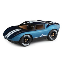 A miniature toy vehicle modelled as a classic American car with metallic blue finish, white racing stripes, and a beige interior. It has a chrome helmeted driver and is equipped with rubber tyres with stylish wheel spinners.