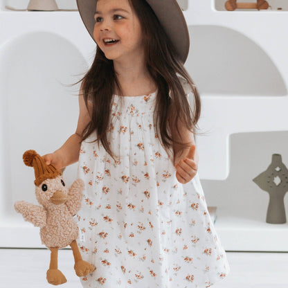 Young girl in a floral dress holding a plush toy, standing against a white background.
