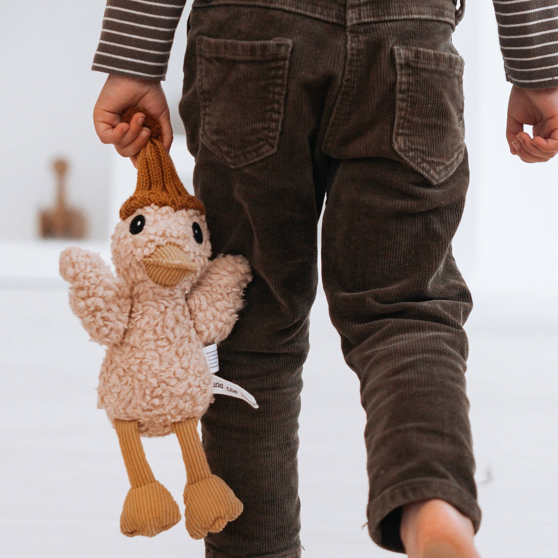 Child holding a knitted duck toy with brown pants on a snowy background