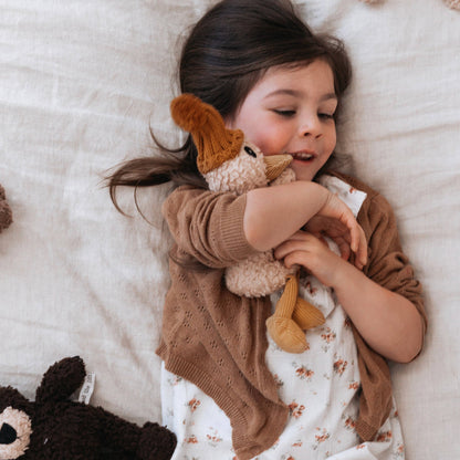 Child lying on a bed holding a stuffed animal, wearing a brown sweater.