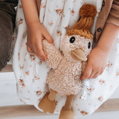 Child holding a knitted duck toy with a brown hat on a floral blanket